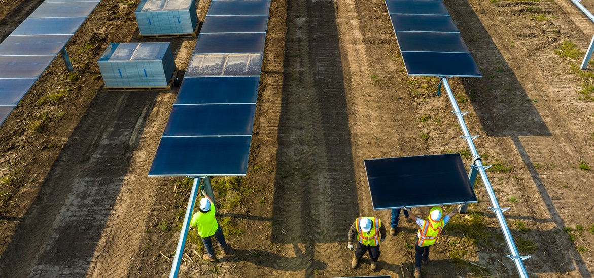 Bird perpective: construction workers installing solar power panels on the field