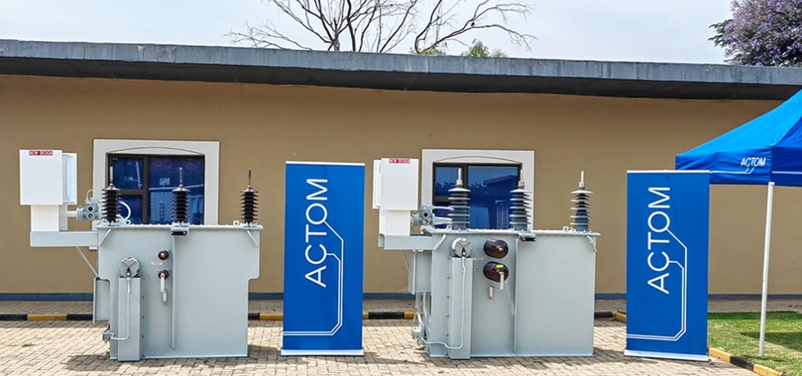 2 power transformers with blue ATCOM banners next to each of them in front of a yellow house