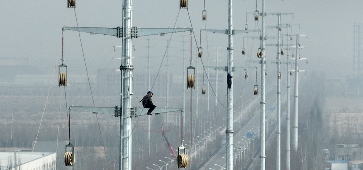 Photo showing a street in Chinese city on a cloudy foggy day and a maintenance worker on top of one of the power towers 