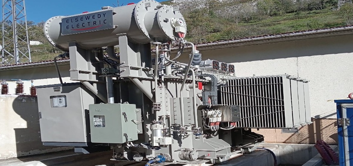 A huge power transformer with Elsewedy Electric logo on it, situated in a substation at the foot of a mountain