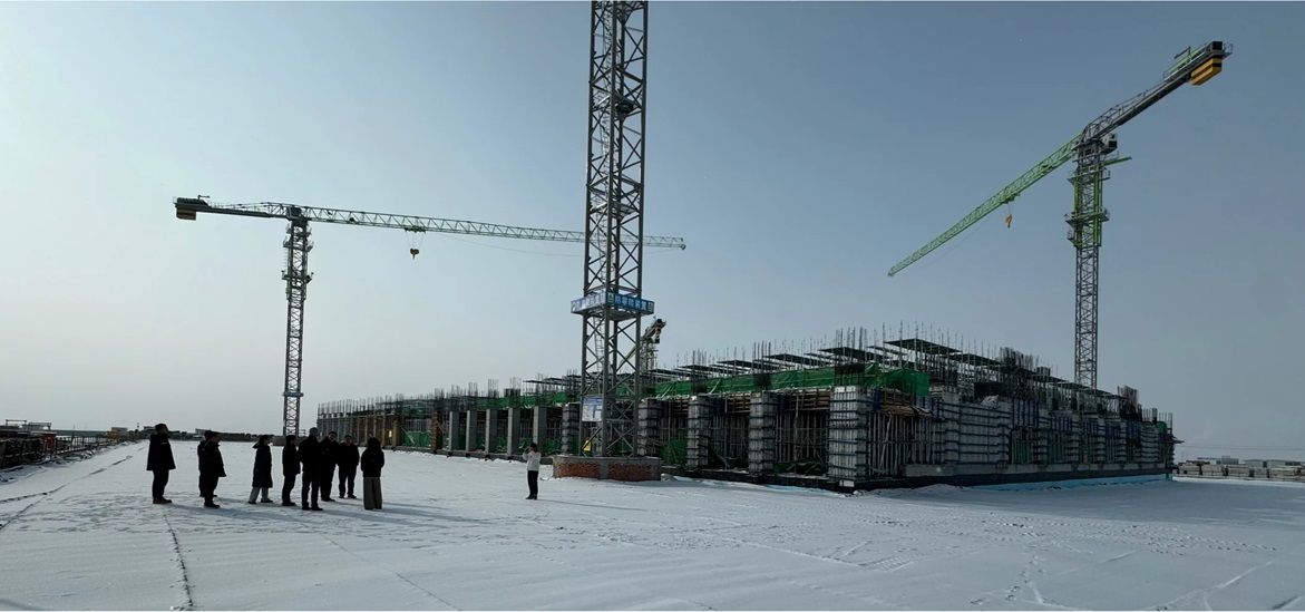 Photo of a construction site in a field covered with snow with a few cranes and a group of people stand in front of it and inspecting it
