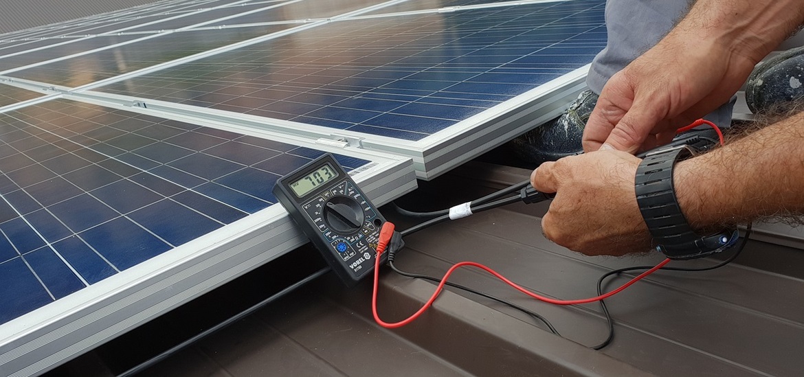 Technician's hands holding a measuring device connected to the solar pannel