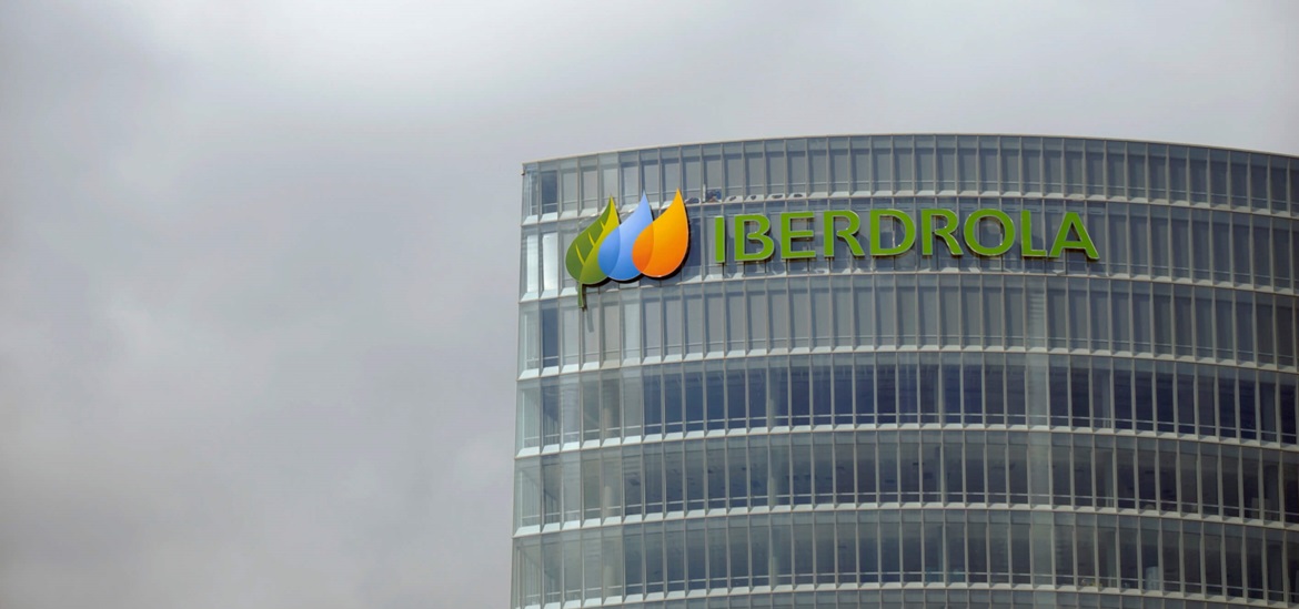 Photo of Iberdrola hedquorter skyscraper pith a company logo at the top, against cloudy grey sky