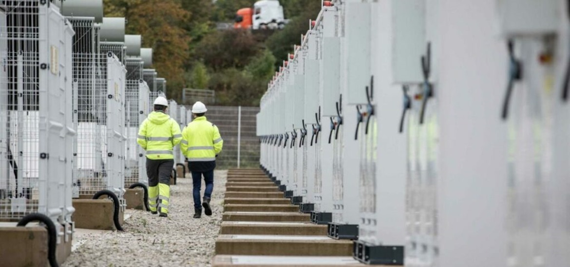 two workers walking on an aisle between two rows of energy storage baterries