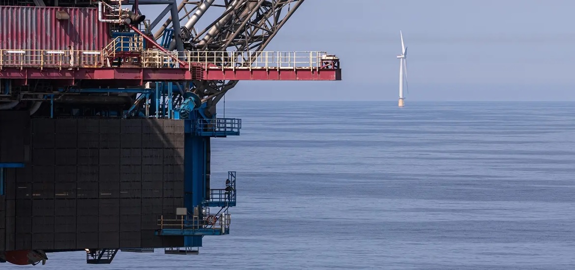 a part of a cargo tanker in front and an offshore wind turbine in the back 