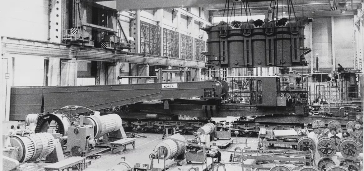 black and white photo of the inside of the factory in finland showing a crane carrying a transformer 