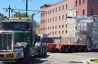 Unloading of a transformer from a green truck in front of a red building