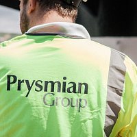 an engineer turning back to the camera with Prysmian logo on his orange vest, talking to his team