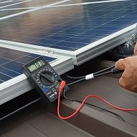 Technician's hands holding a measuring device connected to the solar pannel