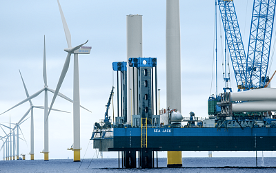 Instalation platform with a crane next to offshore windmills in the middle of the sea
