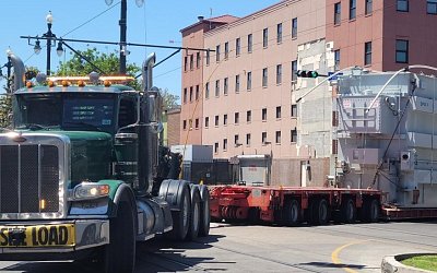 Unloading of a transformer from a green truck in front of a red building